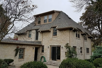 Inspiration for a large timeless beige two-story stone house exterior remodel in Milwaukee with a hip roof and a shingle roof