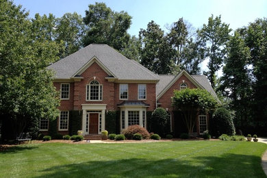 Inspiration for a large timeless red three-story brick house exterior remodel in Charlotte with a shingle roof