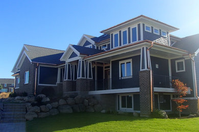 На фото: огромный, синий частный загородный дом в стиле кантри с разными уровнями, комбинированной облицовкой, полувальмовой крышей и крышей из гибкой черепицы с