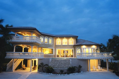 Inspiration for a large mediterranean beige three-story stucco house exterior remodel in Tampa with a hip roof and a tile roof