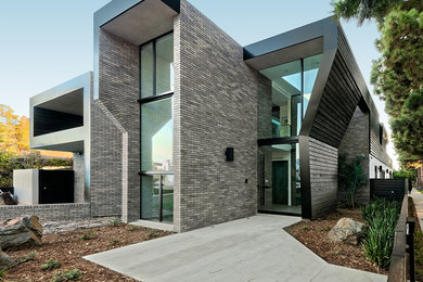 Imagen de fachada de casa gris actual grande de dos plantas con revestimiento de ladrillo y tejado plano