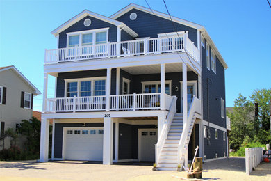 This is an example of a large and blue beach style detached house in New York with three floors, vinyl cladding and a shingle roof.