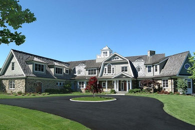 На фото: огромный, двухэтажный, серый дом в классическом стиле с облицовкой из камня и мансардной крышей с