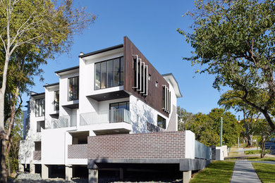 This is an example of an expansive and white modern concrete house exterior in Brisbane with three floors and a flat roof.