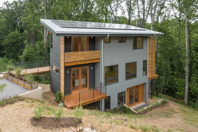 Inspiration pour une façade de maison grise minimaliste en stuc à deux étages et plus avec un toit en appentis et un toit en métal.