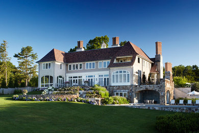 Foto della villa grande beige classica a due piani con rivestimento in stucco, tetto a padiglione e copertura a scandole