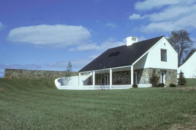 Esempio della facciata di una casa piccola bianca country a due piani con rivestimento in pietra e tetto a capanna