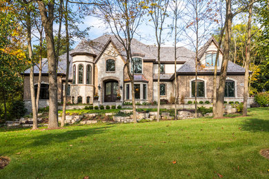 Large traditional beige two-story stone house exterior idea in Chicago with a hip roof and a shingle roof
