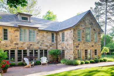 Diseño de fachada de casa beige clásica grande de dos plantas con revestimiento de piedra, tejado a dos aguas y tejado de teja de madera