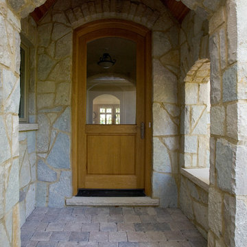 Stone Covered Arch Entry with Glass and Wood Arch Top Front Door and Paver Porch