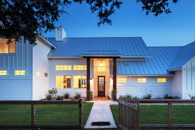 Réalisation d'une grande façade de maison blanche champêtre en bois de plain-pied avec un toit à deux pans et un toit en métal.