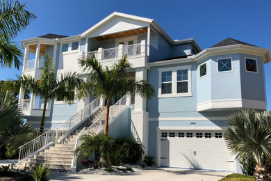 Example of a beach style blue two-story stucco house exterior design in Tampa with a shingle roof
