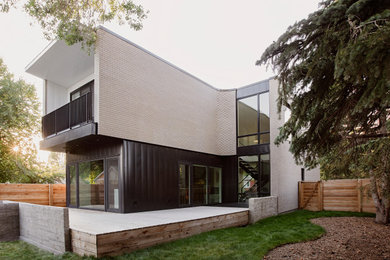 Inspiration for a mid-sized contemporary gray two-story brick exterior home remodel in Calgary with a mixed material roof