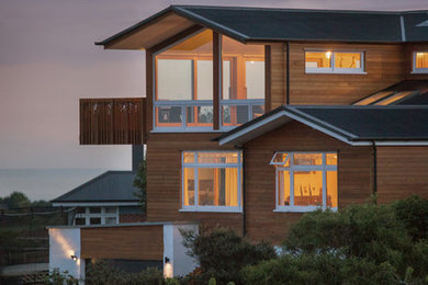 Modelo de fachada de casa multicolor actual grande de tres plantas con revestimiento de madera, tejado a dos aguas y tejado de metal