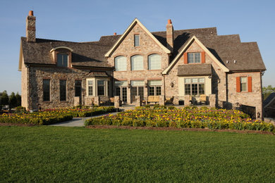 Imagen de fachada de casa gris clásica grande de tres plantas con revestimiento de piedra, tejado a dos aguas y tejado de teja de madera