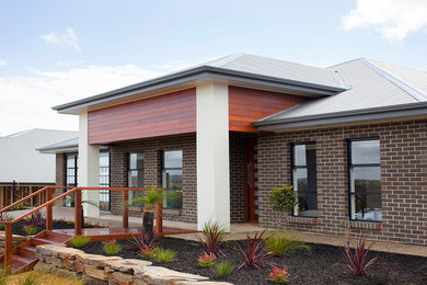 Imagen de fachada de casa actual grande de una planta con revestimiento de ladrillo y tejado de metal