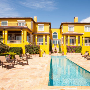 Imagen de fachada de casa amarilla, mediterránea, extra grande, de tres plantas, con revestimiento de estuco, tejado a cuatro aguas y tejado de teja de barro