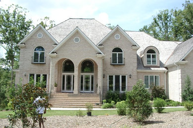 Ejemplo de fachada beige tradicional grande de dos plantas con revestimiento de ladrillo y tejado a dos aguas