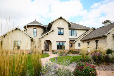 Idée de décoration pour une grande façade de maison beige méditerranéenne en pierre à un étage.