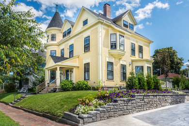 На фото: трехэтажный, желтый дом в викторианском стиле с двускатной крышей с