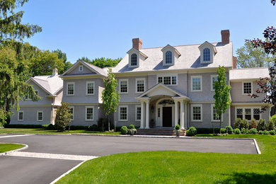 Esempio della villa grande bianca classica a due piani con rivestimento in legno, tetto a mansarda e copertura a scandole
