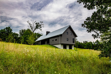 Cette photo montre une façade de maison grise nature à un étage avec un toit à deux pans et un toit en métal.
