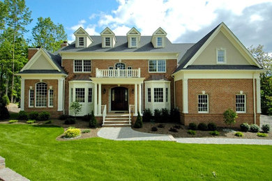 Aménagement d'une grande façade de maison rouge classique en brique à un étage avec un toit à deux pans et un toit en shingle.