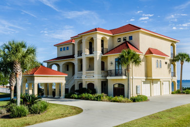 Large elegant yellow three-story stucco house exterior photo in Miami with a clipped gable roof and a tile roof