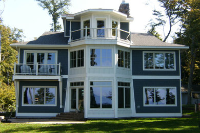 Example of a large beach style blue three-story wood house exterior design in Grand Rapids with a hip roof and a shingle roof