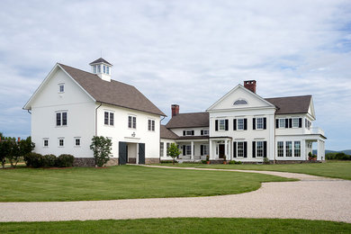 Esempio della villa grande bianca country a due piani con rivestimento in legno, tetto a capanna e copertura a scandole