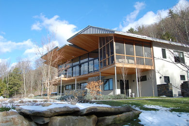 Cette image montre une grande façade de maison grise minimaliste en stuc à un étage avec un toit à croupette et un toit en métal.