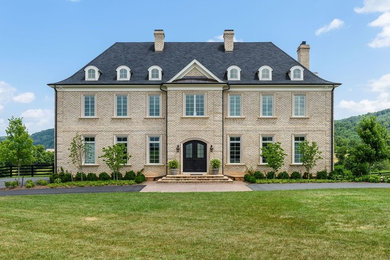 Example of a large classic beige two-story stone house exterior design in Other with a clipped gable roof and a shingle roof