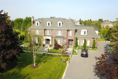 Foto della villa grande marrone classica a due piani con rivestimento in mattoni, tetto a mansarda e copertura a scandole