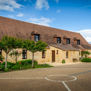 Réalisation d'une façade de maison beige champêtre à un étage avec un toit à quatre pans et un toit en tuile.