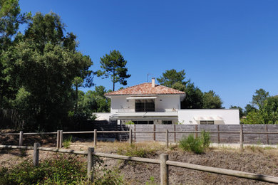 Cette photo montre une grande façade de maison blanche tendance en béton à un étage avec un toit à quatre pans et un toit en tuile.