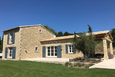 Réalisation d'une façade de maison beige méditerranéenne en pierre à un étage avec un toit à deux pans et un toit en tuile.