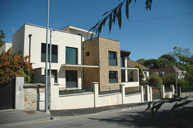 Cette photo montre une grande façade de maison beige moderne à deux étages et plus avec un revêtement mixte et un toit plat.