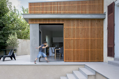 Cette image montre une petite façade de maison beige design en bois à un étage avec un toit en appentis et un toit mixte.