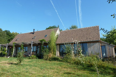 Cette image montre une façade de maison marron rustique en bois de taille moyenne et à un étage avec un toit à deux pans et un toit en tuile.