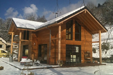 Cette image montre une petite façade de maison marron minimaliste en bois à un étage avec un toit de Gambrel et un toit en tuile.