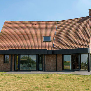 Aménagement d'une grand façade de maison rouge contemporaine à un étage avec un toit à deux pans et un toit en tuile.