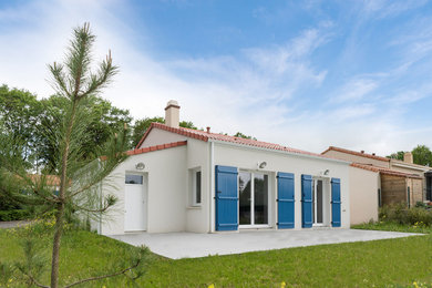 Cette photo montre une façade de maison blanche chic en béton de plain-pied avec un toit à deux pans et un toit en tuile.