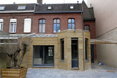 This is an example of a large and red contemporary house exterior in Lille with three floors, wood cladding, a lean-to roof and a metal roof.