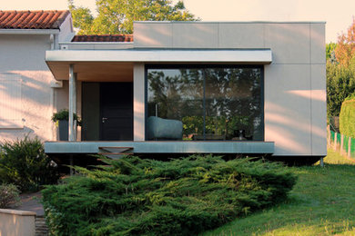 Modern inredning av ett mellanstort beige hus, med två våningar, fiberplattor i betong och platt tak