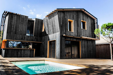 Cette image montre une façade de maison noire minimaliste en bois à un étage avec un toit en métal et un toit noir.