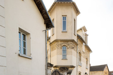 Cette image montre une façade de maison de ville beige traditionnelle en pierre à deux étages et plus avec un toit à quatre pans et un toit en tuile.