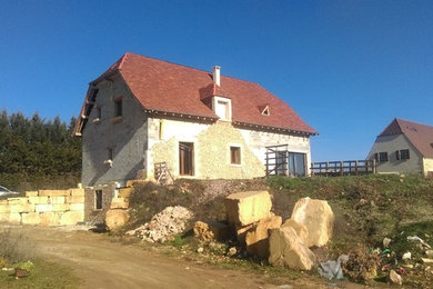 Réalisation d'une grande façade de maison beige champêtre en pierre à un étage avec un toit à croupette et un toit en tuile.