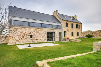 Réalisation d'une très grande façade de maison blanche champêtre en pierre à deux étages et plus avec un toit à deux pans et un toit mixte.