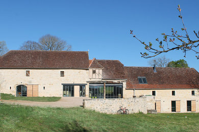 Réalisation d'une grande façade de maison beige champêtre en pierre à deux étages et plus avec un toit à deux pans.