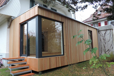 Foto della villa piccola beige contemporanea a un piano con rivestimento in legno, tetto piano e copertura verde